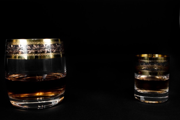 Krótka szklanka i kieliszek ciemnej czerwonej whisky brandy lub xAbourbon na białym tle na czarnym tle Zbliżenie zdjęcie alkoholu