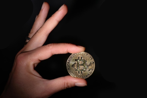 Kryptowaluta Bit Coin trzymana między palcami na czarnym tle