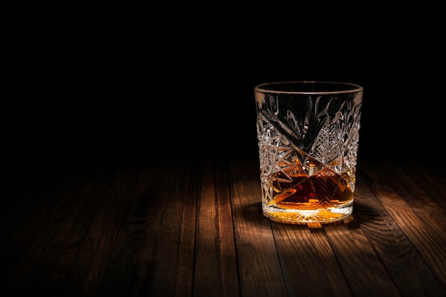Krystaliczny szkło z whisky i przekąskami na drewnianym stole na czarnym tle