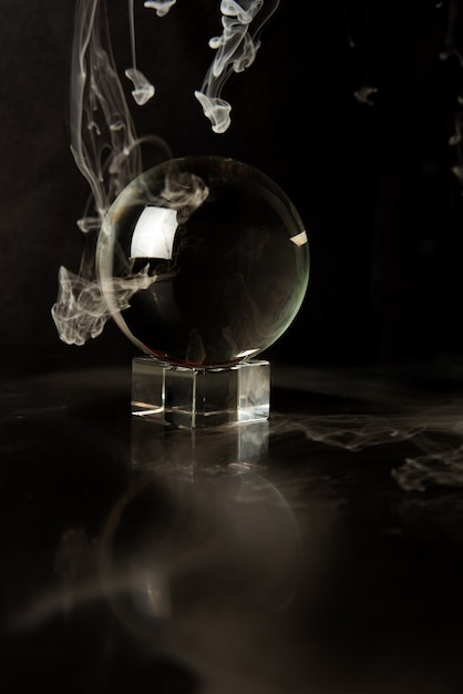Kryształowa kula odbijająca czarne tło i spadający dym, selektywne focus.