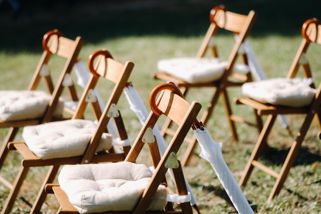 Zdjęcie krzesła stoją na zielonej trawie na terenie ceremonii zaślubin, na krzesłach wiszą białe parasole