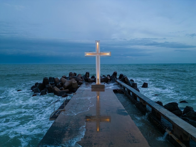 Krzyż chrześcijański stojący na molo w morzu lub oceanie z dramatycznym niebem w nocy