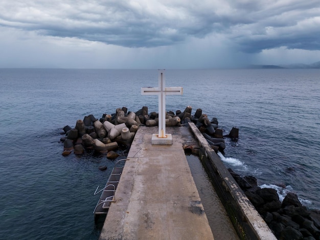 Krzyż chrześcijański stojący na molo w morzu lub oceanie z dramatycznym niebem