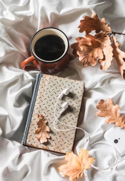 Książka do kawy słuchawki telefon na łóżku widok z góry Wypoczynek przytulny koncept domu Ciepły jesienny nastrój