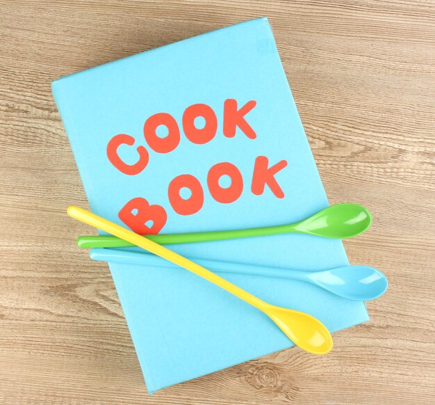 Książka kucharska i przybory kuchenne na drewnianym tle