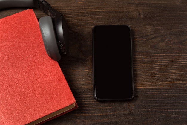 Książka, smartfon i słuchawki na stole