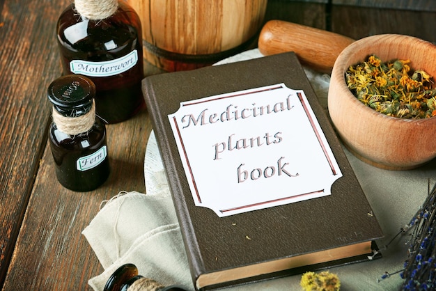 Książka z roślinami leczniczymi z suszonymi ziołami i butelkami na stole