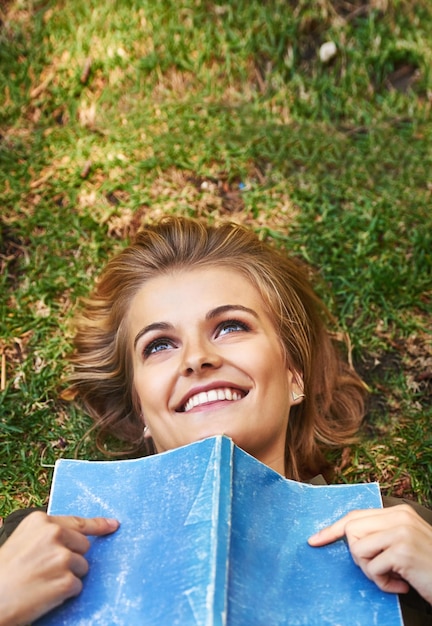 Książki mogą naprawdę poruszyć twój umysł Zdjęcie atrakcyjnej młodej kobiety czytającej książkę leżącej na zewnątrz na trawie