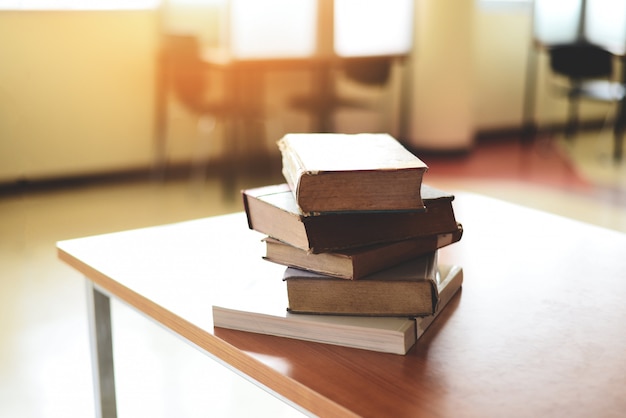 Książki na stole w bibliotece - edukacja uczy się książkową stertę na drewnianym biurku i zamazanym izbowym tle, z powrotem szkoły pojęcie