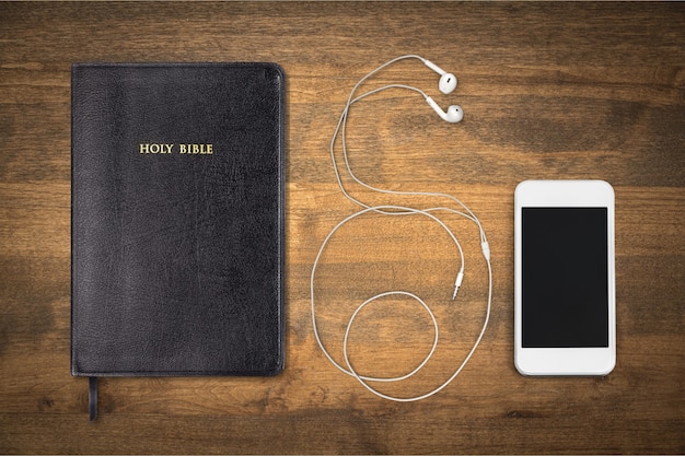 Księga Pisma Świętego i smartfon ze słuchawkami w tle