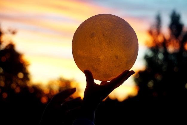 Księżyc w dłoni na tle czerwony wschód słońca. Księżycowa lampka nocna na niebie