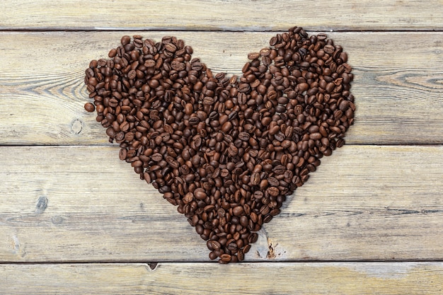 Kształt serca wykonany z ziaren kawy na powierzchni drewnianej.