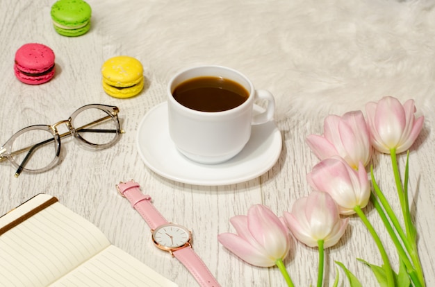 Kubek do kawy, okulary przeciwsłoneczne, zegarki, notatnik i różowe tulipany na stole. Koncepcja pracy.