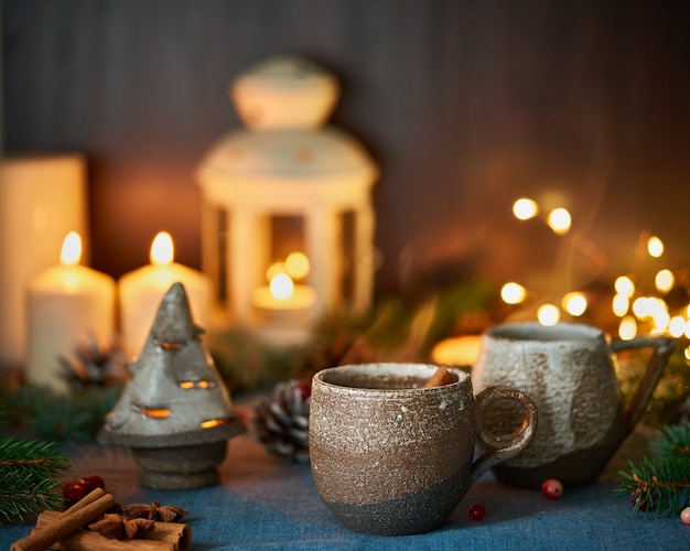 Kubek gorącego napoju na tle Bożego Narodzenia. Przytulny wieczór, kubek grzanego wina, dekoracje świąteczne, świece i girlandy świetlne.