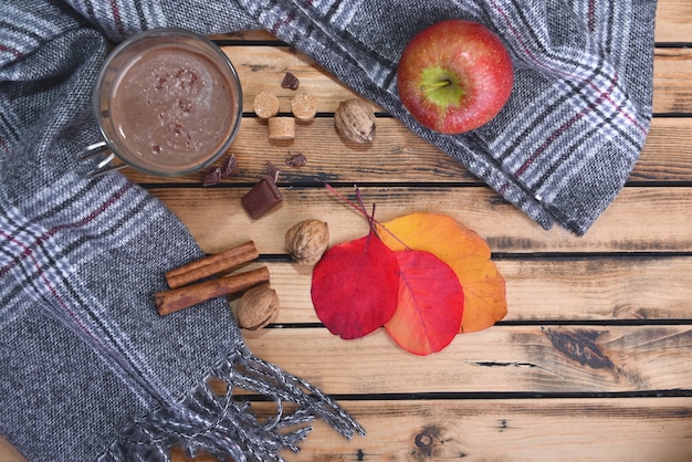 Kubek gorącej czekolady z szalikiem i czerwonym jabłkiem zimą i na drewnianym stole
