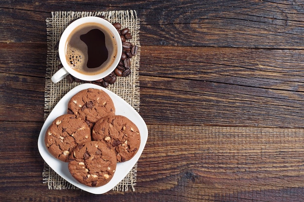Kubek gorącej kawy i czekoladowe ciasteczka z orzechami na drewnianym stole, widok z góry