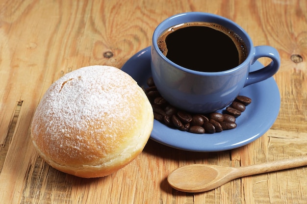 Kubek gorącej kawy ze słodkim pączkiem na śniadanie na starym drewnianym stole