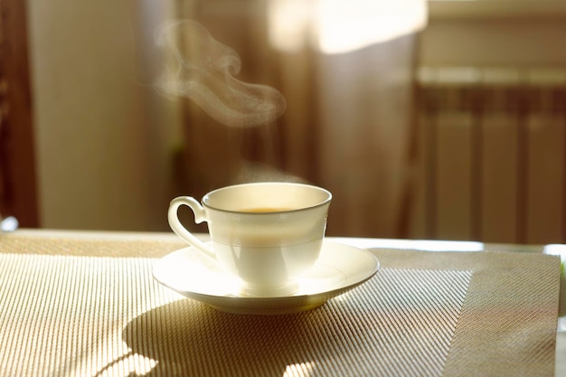 Kubek gorącej parującej kawy w słoneczny poranek na kuchennym stole