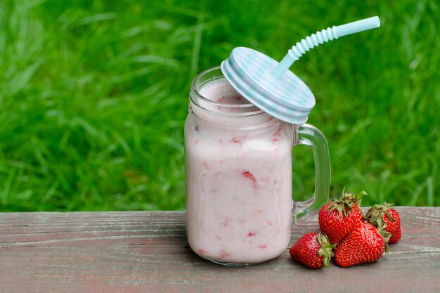 Kubek jogurt i truskawka na zielonej trawie