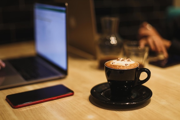 Kubek kawy latte art w kształcie uroczego kota z laptopem w tle.