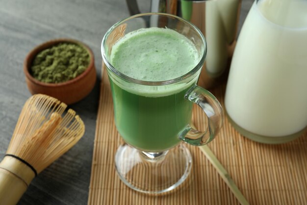 Kubek matcha latte i akcesoria do robienia na szarym teksturowanym stole