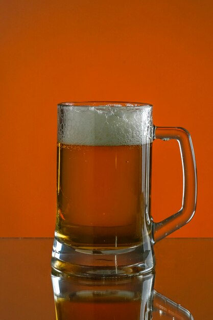 Kubek piwa odbity na stole i na pomarańczowym tle Skopiuj miejsce