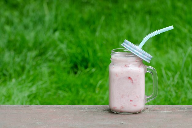 Kubek truskawkowy jogurt na tle zielona trawa