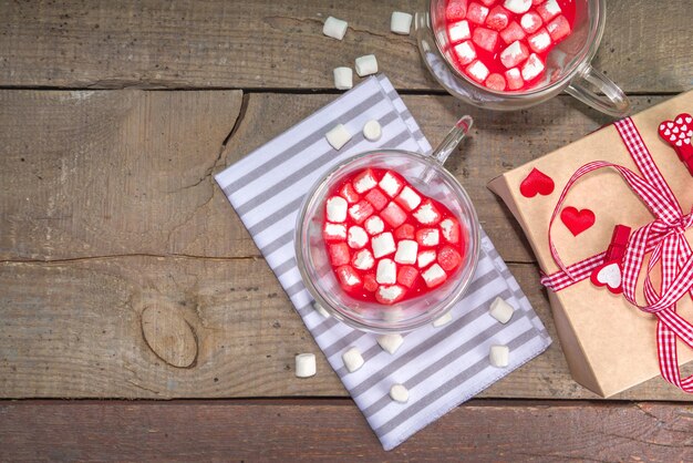 Kubek w kształcie serca z czerwoną aksamitną gorącą czekoladą, z małymi piankami, pudełkiem prezentowym i kwiatami na Walentynki