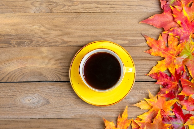 kubek z gorącą czarną kawą na drewnianym stole z opadłymi jesienią żółtymi, pomarańczowymi i czerwonymi liśćmi