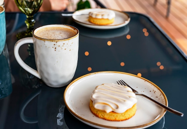Kubek z kawą cappuccino lub latte i wegańskim ciastem deserowym na niebieskim tle światła na szklanym stole