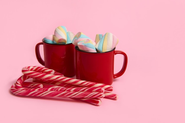 Kubki do kawy z marshmallows i cukierkami na różowym kolorowym tle. Świąteczny gorący napój z deserami. Gorąca czekolada, filiżanka kawy kakaowej. Nowy rok, Wesołych Świąt Bożego Narodzenia obchody