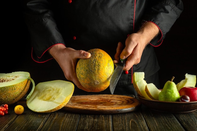 Kucharz cięje dojrzały melon nożem na drewnianej desce na kuchennym stole.