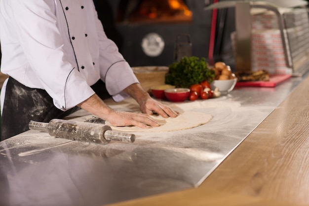 kucharz przygotowujący ciasto na pizzę wałkuje rękami na posypanym mąką stole