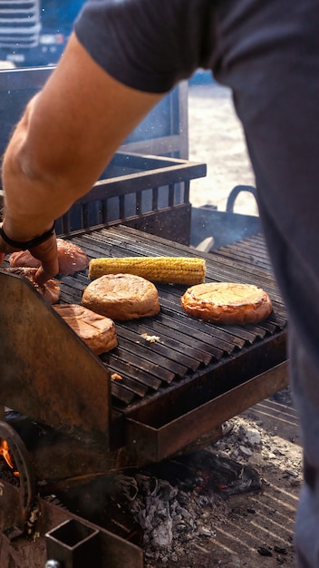 Kucharz smażący kolby kukurydzy i bułki do hamburgerów na grillu. Ciężarówka z żywnością. Uliczne jedzenie