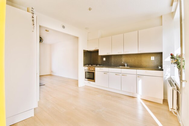 Zdjęcie kuchnia i jadalnia w mieszkaniu z białymi szafami, drewnianą podłogą i żółtymi drzwiami prowadzącymi do salonu