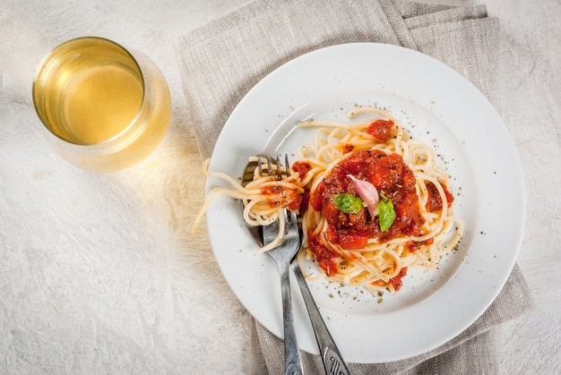 Kuchnia włoska. Lunch lub kolacja Porcja makaronu spaghetti z pomidorowym sosem marinara i bazylią na białym betonowym stole. Przy lampce białego wina. Skopiuj widok z góry