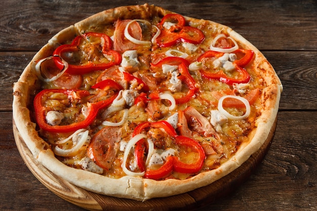 Kuchnia włoska, tradycyjne fast foody. Apetyczna kolorowa świeża pizza z szynką, serem, pomidorem, papryką i cebulą na rustykalnym drewnianym stole, widok z góry.