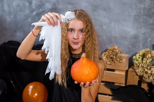 Kudłata nastolatka wśród wystroju w odcieniach czerni i pomarańczy na święta Halloween z duchem w rękach