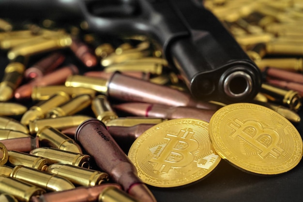 Kule z brązu i mosiądzu rozrzucone na ciemnym stole, czarna lufa pistoletu, złote monety bitcoin w pobliżu - nielegalne użycie kryptowaluty do zakupu koncepcji broni