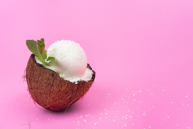 Kulka lodów waniliowych w świeżym kokosie w połowie ozdobiona liśćmi mięty na różowym tle