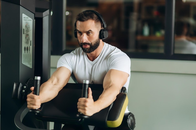 Kulturysta mężczyzna robi ćwiczenia w klubie fitness Facet ma na sobie białą koszulkę Fitness koncepcja zdrowego stylu życia