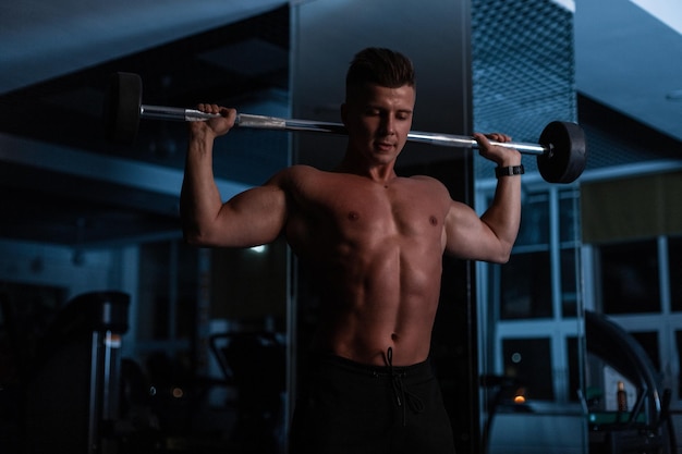 Kulturysta mężczyzna sportowiec z muskularnym ciałem robi ćwiczenia w hali na ciemnoniebieskim tle
