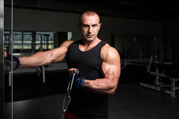 Kulturysta mięśni fitness wykonujący ciężkie ćwiczenia na biceps na maszynie z kablem na siłowni