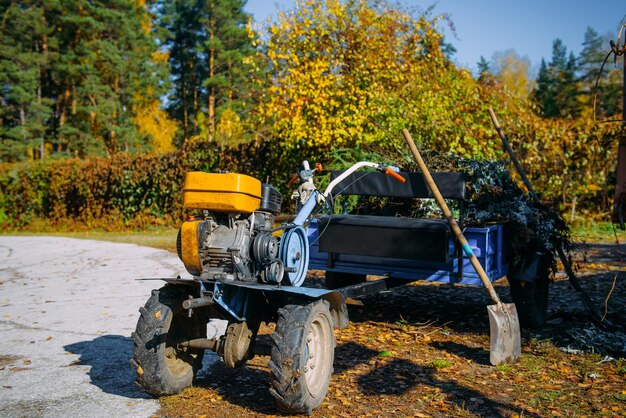 Zdjęcie kultywator motocyklowy stojący na tle drzew z zielonymi i żółtymi liśćmi. jesień pracuje nad poprawą terenu ogrodu botanicznego.