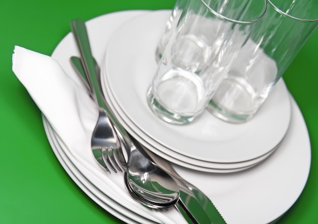 Kupie białe talerze, szklanki z widelcami i łyżkami na jedwabnej serwetce. Zielone tło