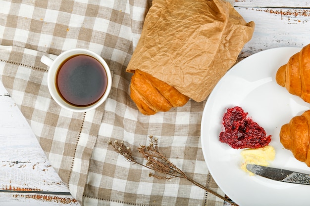 Kurasan z masłem i dżemem. początek poranka. Kubek kawy. Świeży francuski rogalik. Filiżanka i świezi piec croissants na drewnianym tle. Widok z góry.