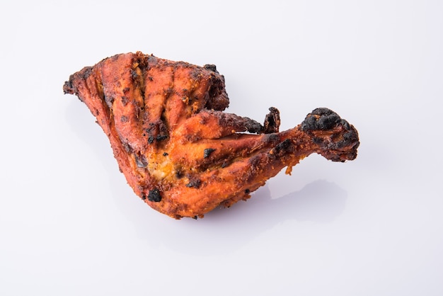 Kurczak Tandoori - przygotowywany przez pieczenie kurczaka marynowanego w jogurcie i przyprawach w piecu tandoor. Kawałek nogi podawany w talerzu z sałatką na kolorowym lub drewnianym tle. Selektywne skupienie