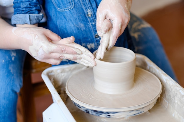 Kursy ręcznie robionej ceramiki dla hobby. klasa mistrzowska w warsztacie. garncarz formujący glinę na obracającym się kole z małym uczniem