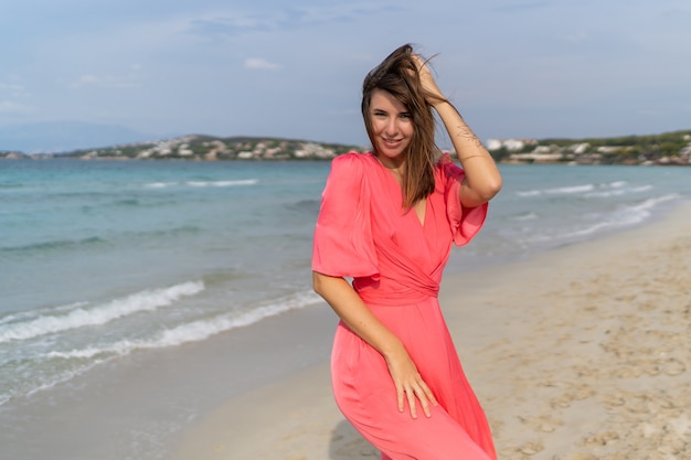 Kusząca brunetka dama z tatuażem pod ręką w różowej sukience pozowanie na plaży.