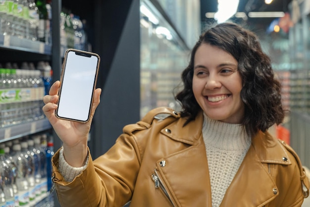 Kusząca kobieta trzyma biały ekran telefonu w sklepie spożywczym